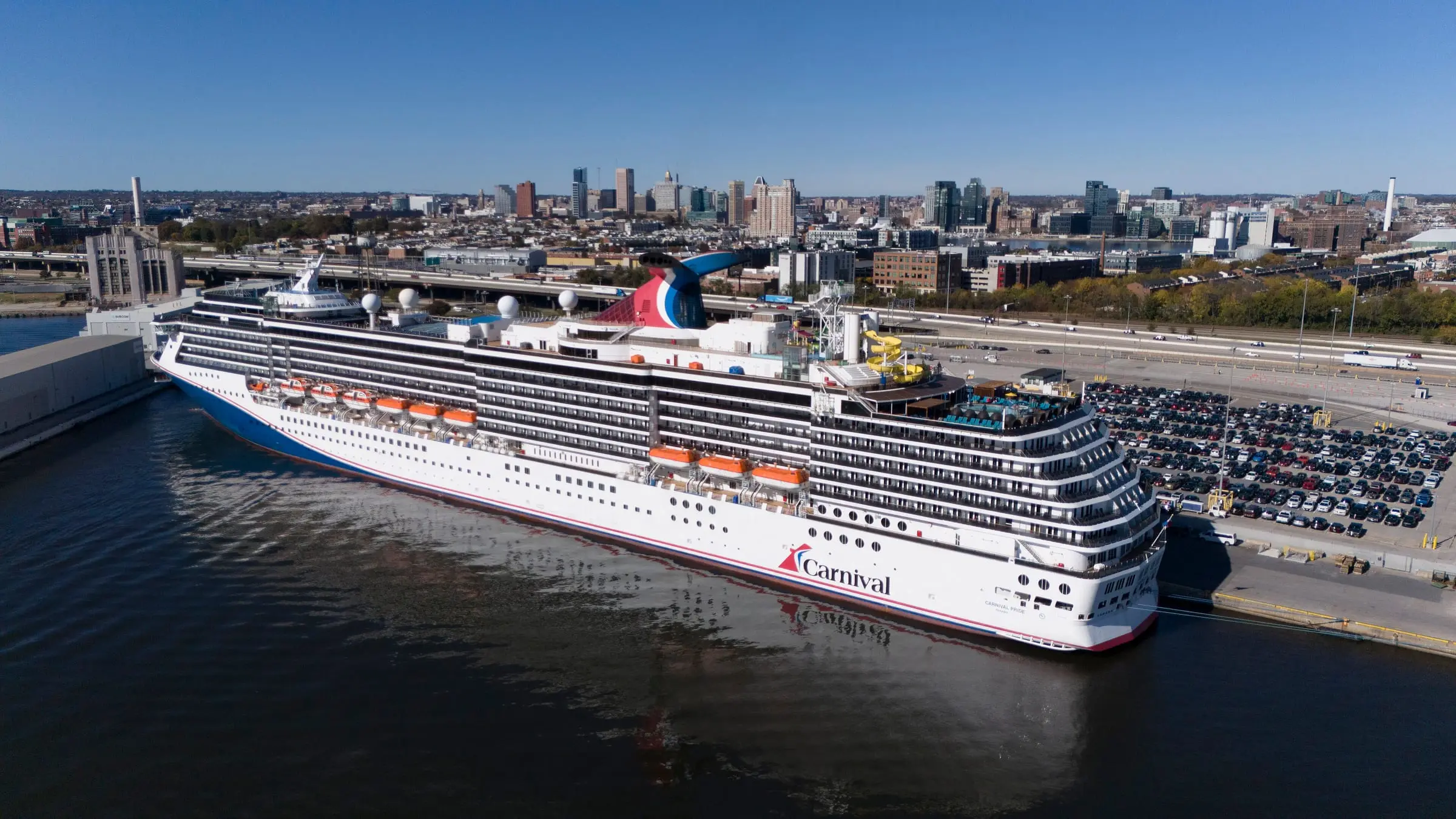 Carnival Pride docked at the Cruise Maryland Terminal in South Locust Point, seen from the air, with the Baltimore skyline behind